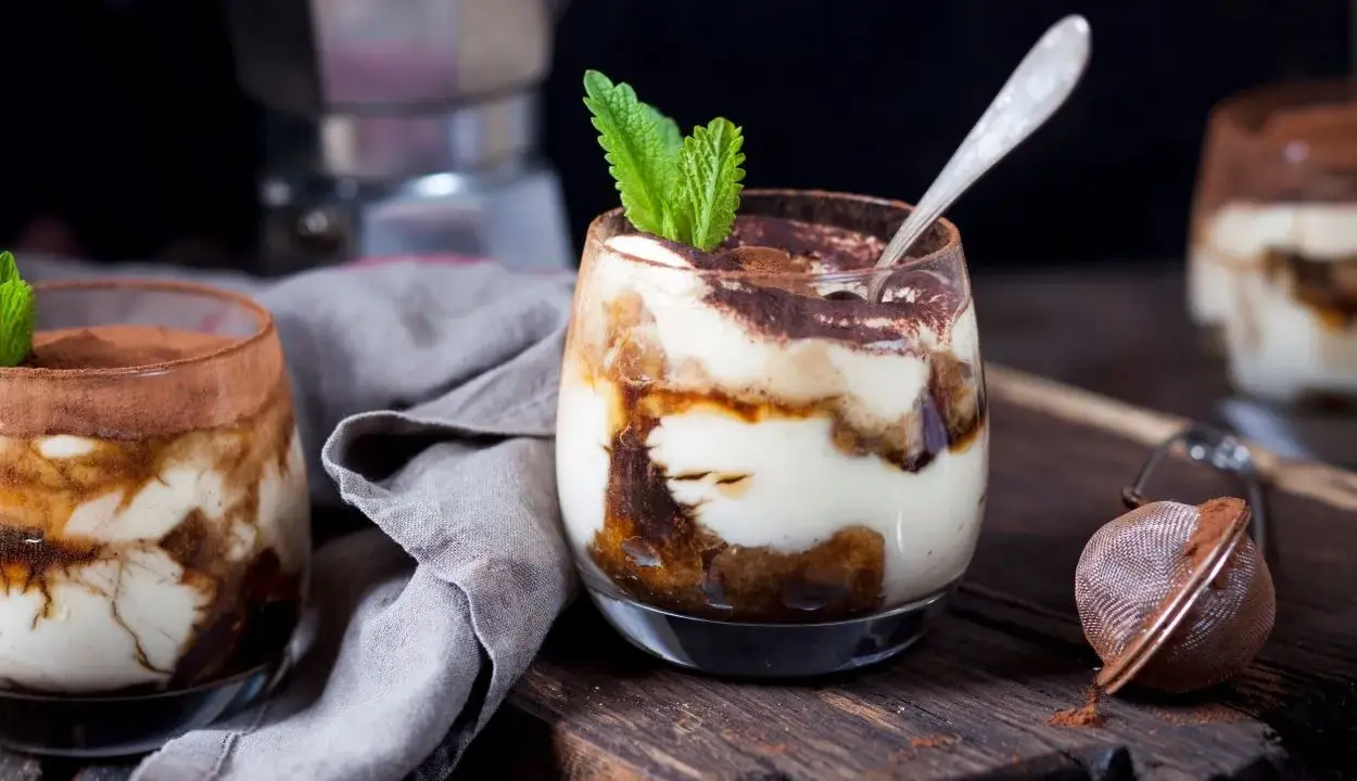 Pyszne tiramisu w pucharkach, udekorowane listkiem mięty, czeka na spróbowanie.