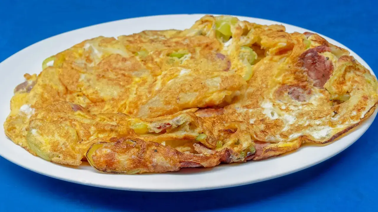 Złocisty omlet na słono z kawałkami kiełbasy i warzyw, podany na białym talerzu.