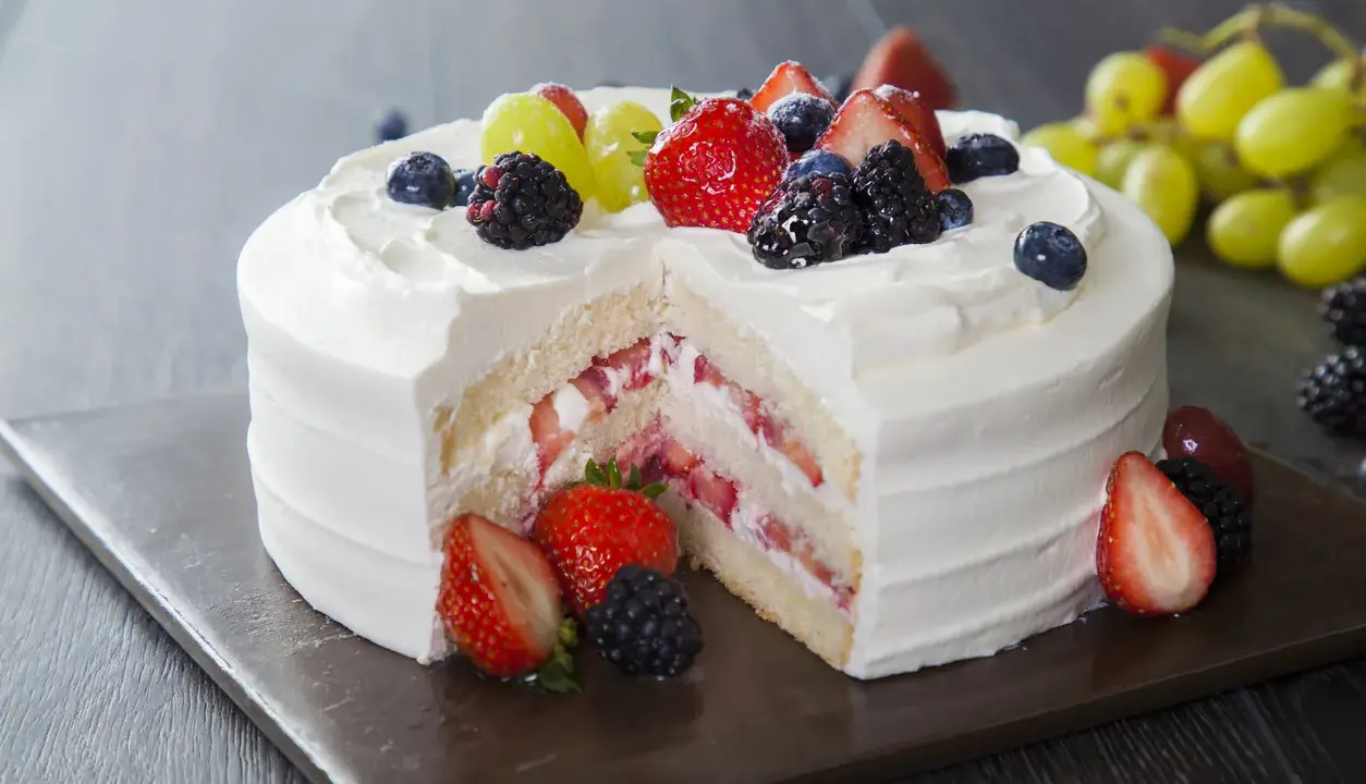 Pyszny tort z bitą śmietaną i serkiem mascarpone, przełożony świeżymi truskawkami i udekorowany owocami leśnymi.
