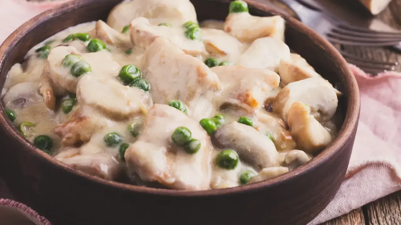 Pyszny strogonow z kurczaka z pieczarkami i groszkiem w kremowym sosie, podany w glinianej misce na drewnianym stole.