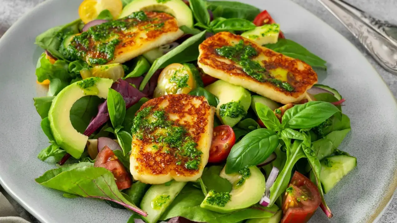 Pyszna sałatka z halloumi, awokado, pomidorkami i ogórkiem, polana zielonym sosem.