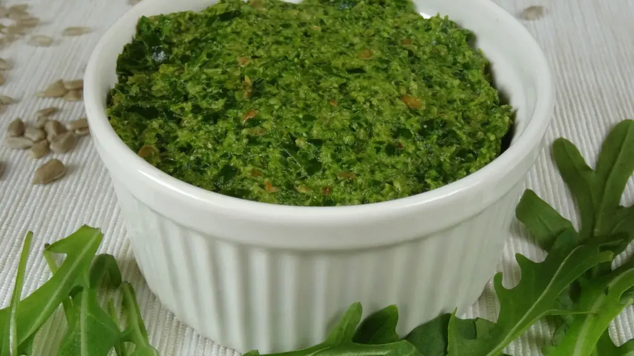 Domowe pesto z rukoli, pełne świeżości i aromatu, w białej miseczce. Obok świeże liście rukoli i nasiona słonecznika.