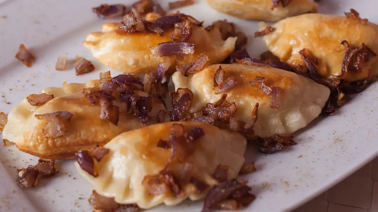 Pyszne pierogi z mięsem, okraszone chrupiącą cebulką, kuszą na białym talerzu.