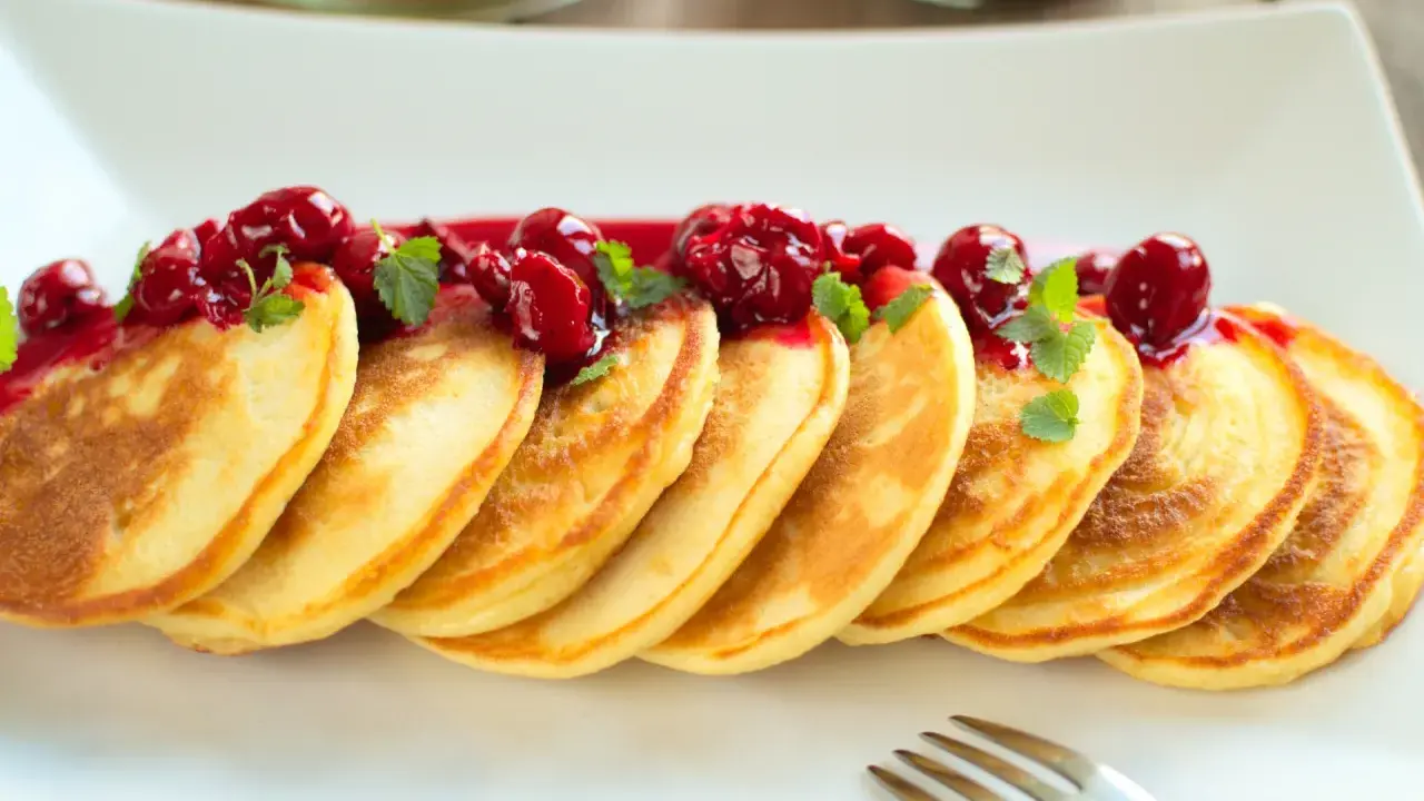 Puszyste pancakes na maślance, polane wiśniowym sosem i ozdobione listkami mięty. Idealne na słodkie śniadanie.