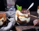 Pyszne tiramisu w pucharkach, udekorowane listkiem mięty, czeka na spróbowanie.