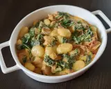 Pyszne gnocchi z kurczakiem w kremowym sosie ze szpinakiem i suszonymi pomidorami. Danie podane w białej miseczce.