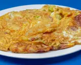 Złocisty omlet na słono z kawałkami kiełbasy i warzyw, podany na białym talerzu.