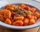 Pyszne gnocchi w sosie pomidorowym, posypane świeżą bazylią, podane w talerzu z niebieskim rantem.