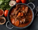 Gęsty, aromatyczny gulasz z sarny w sosie z warzywami. Obok naczynia miseczki z przyprawami i świeże pomidory.
