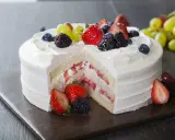 Pyszny tort z bitą śmietaną i serkiem mascarpone, przełożony świeżymi truskawkami i udekorowany owocami leśnymi.