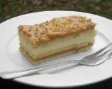 Pyszne ciasto 3 bit z kremem i orzechami na białym talerzu, obok widelec.