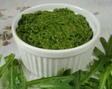 Domowe pesto z rukoli, pełne świeżości i aromatu, w białej miseczce. Obok świeże liście rukoli i nasiona słonecznika.
