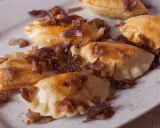 Pyszne pierogi z mięsem, okraszone chrupiącą cebulką, kuszą na białym talerzu.