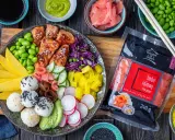 Kolorowy bowl z lososiem, ryżem, mango, awokado, edamame i marynowanym imbirem. Obok opakowanie imbiru różowego.
