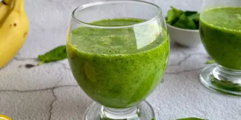 Zielony koktajl ze szpinakiem w szklance, obok banan i cytryna. Pyszny i zdrowy napój.