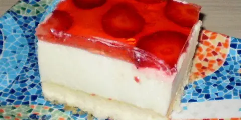 Tradycyjny sernik na zimno z serków homogenizowanych, z galaretką i owocami, na kolorowym talerzyku.