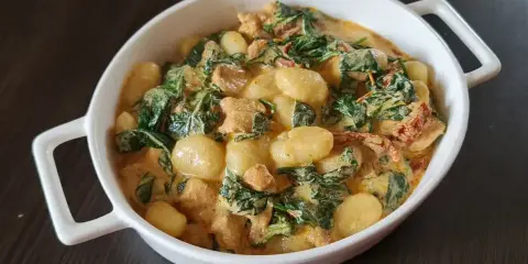 Pyszne gnocchi z kurczakiem w kremowym sosie ze szpinakiem i suszonymi pomidorami. Danie podane w białej miseczce.