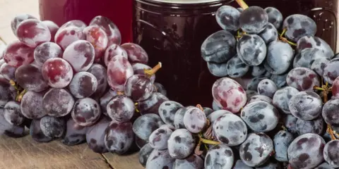 Słoiki z domowym dżemem z winogron, obok świeże kiście ciemnych i czerwonych winogron na drewnianym stole.