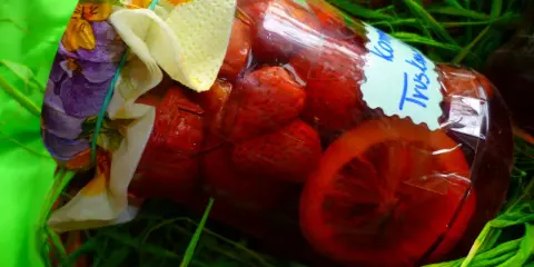 Słoik z domowym kompotem z truskawek, ozdobiony kolorową tkaniną i etykietą.