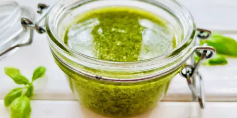 Słoiczek pełen aromatycznego pesto z bazylii, obok świeże listki. Idealne do makaronu i kanapek.