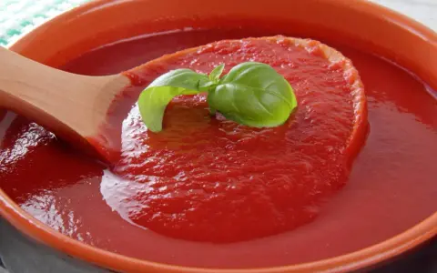 Gęsty, domowy ketchup z pomidorów, z listkiem bazylii na drewnianej łyżce. Idealny przepis na lato!