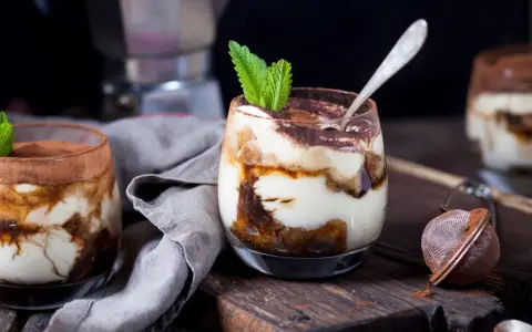 Pyszne tiramisu w pucharkach, udekorowane listkiem mięty, czeka na spróbowanie.