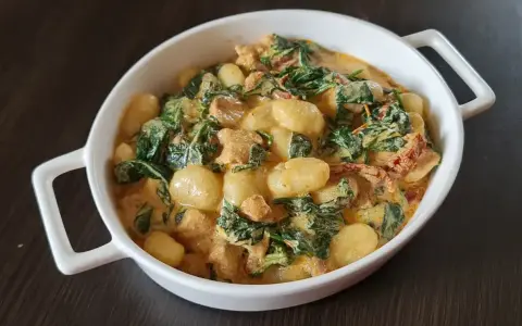 Pyszne gnocchi z kurczakiem w kremowym sosie ze szpinakiem i suszonymi pomidorami. Danie podane w białej miseczce.