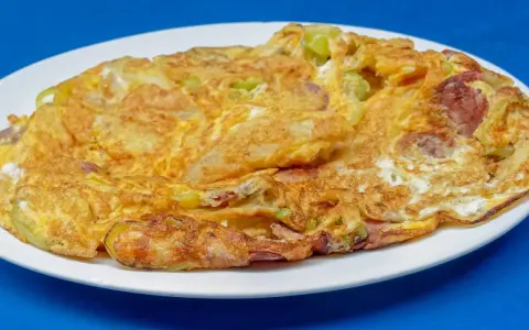Złocisty omlet na słono z kawałkami kiełbasy i warzyw, podany na białym talerzu.