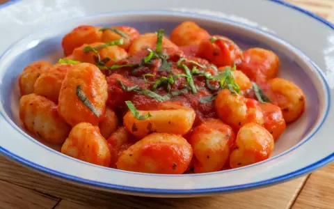 Pyszne gnocchi w sosie pomidorowym, posypane świeżą bazylią, podane w talerzu z niebieskim rantem.