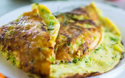 Złocisty omlet z cukinią, lekko przypieczony, podany na białym talerzu.