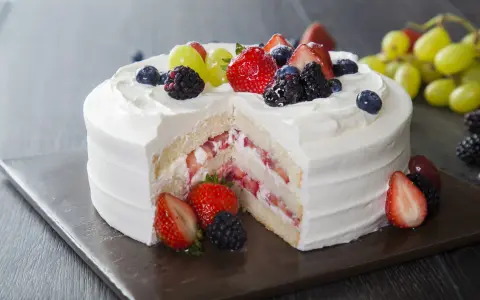 Pyszny tort z bitą śmietaną i serkiem mascarpone, przełożony świeżymi truskawkami i udekorowany owocami leśnymi.