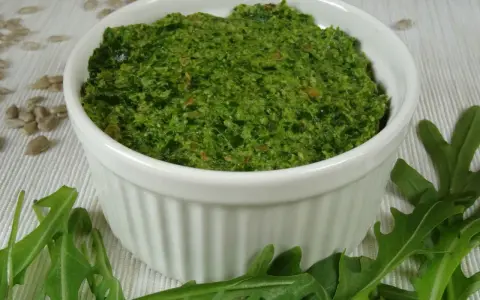 Domowe pesto z rukoli, pełne świeżości i aromatu, w białej miseczce. Obok świeże liście rukoli i nasiona słonecznika.