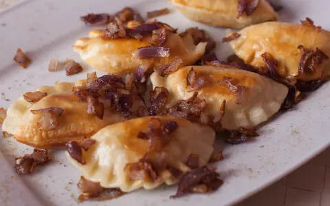 Pyszne pierogi z mięsem, okraszone chrupiącą cebulką, kuszą na białym talerzu.