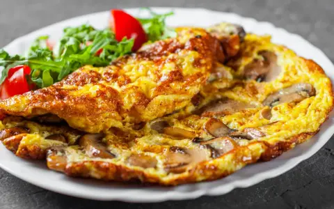 Złocisty omlet z pieczarkami, podany z sałatką z rukoli i pomidorków. Pyszne śniadanie gotowe!