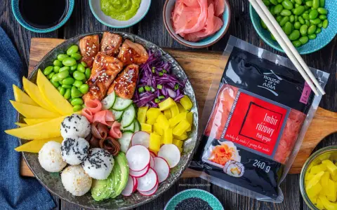 Kolorowy bowl z lososiem, ryżem, mango, awokado, edamame i marynowanym imbirem. Obok opakowanie imbiru różowego.
