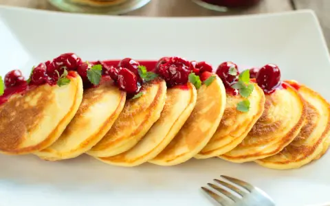 Puszyste pancakes na maślance, polane wiśniowym sosem i ozdobione listkami mięty. Idealne na słodkie śniadanie.