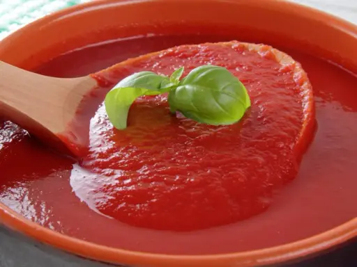 Gęsty, domowy ketchup z pomidorów, z listkiem bazylii na drewnianej łyżce. Idealny przepis na lato!