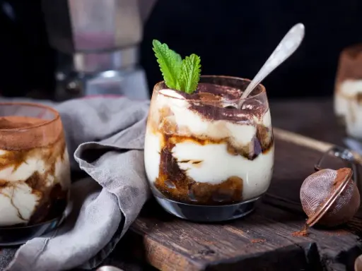Pyszne tiramisu w pucharkach, udekorowane listkiem mięty, czeka na spróbowanie.