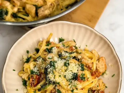 Makaron z kurczakiem w kremowym sosie, szpinakiem i suszonymi pomidorami. Danie "marry me chicken" posypane parmezanem.
