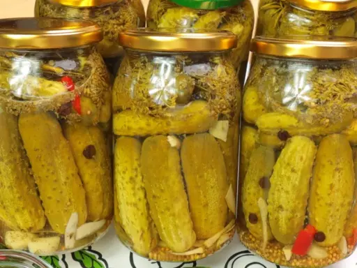 Słoiki z ogórkami kiszonymi, idealne na przepis na ogórki w occie. Widać przyprawy, czosnek i chili.