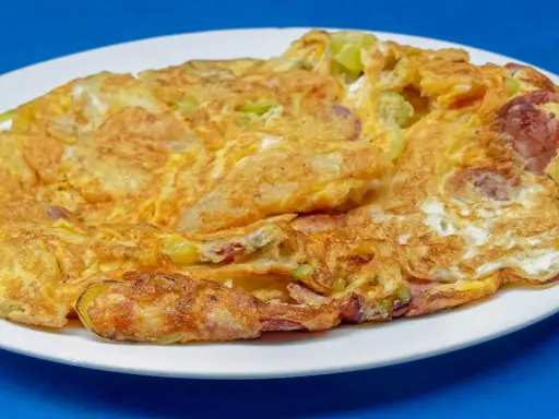 Złocisty omlet na słono z kawałkami kiełbasy i warzyw, podany na białym talerzu.