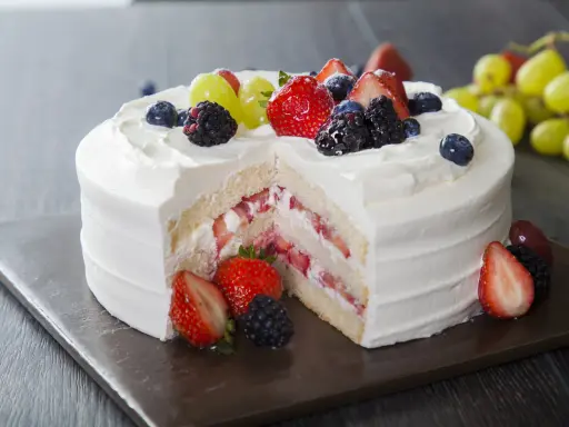 Pyszny tort z bitą śmietaną i serkiem mascarpone, przełożony świeżymi truskawkami i udekorowany owocami leśnymi.