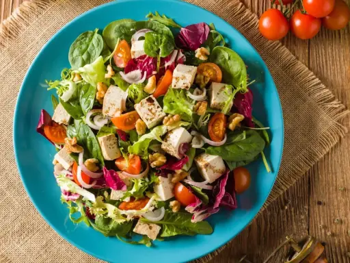 Kolorowa sałatka z kostkami grillowanego tofu, pomidorkami koktajlowymi, orzechami i świeżymi liśćmi sałat.