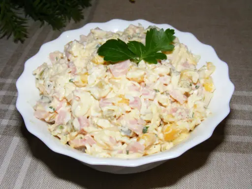 Pyszna sałatka na Wielkanoc z szynką, jajkiem i kukurydzą, udekorowana natką pietruszki.