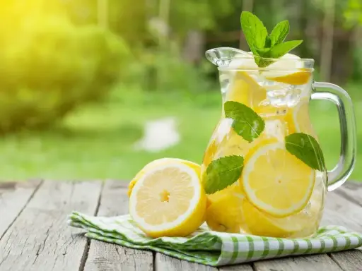 Jak zrobić dobrą lemoniadę? Orzeźwiający dzbanek z cytrynami, lodem i miętą na drewnianym stole w ogrodzie.