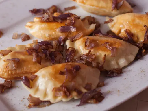 Pyszne pierogi z mięsem, okraszone chrupiącą cebulką, kuszą na białym talerzu.