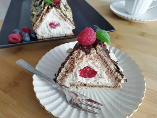 Trójkątny deser z kremem i wiśnią w środku, przypominający chatkę Baby Jagi. Udekorowany owocami i płatkami migdałów.