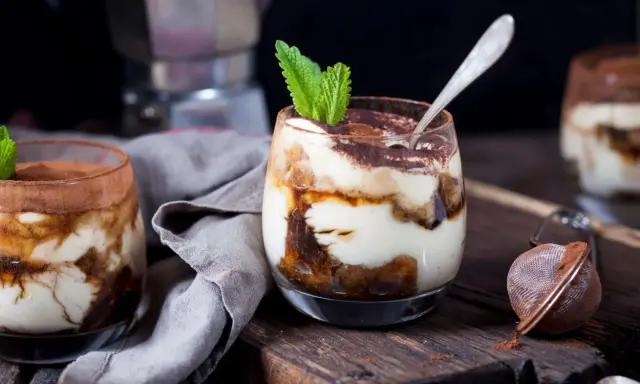 Pyszne tiramisu w pucharkach, udekorowane listkiem mięty, czeka na spróbowanie.