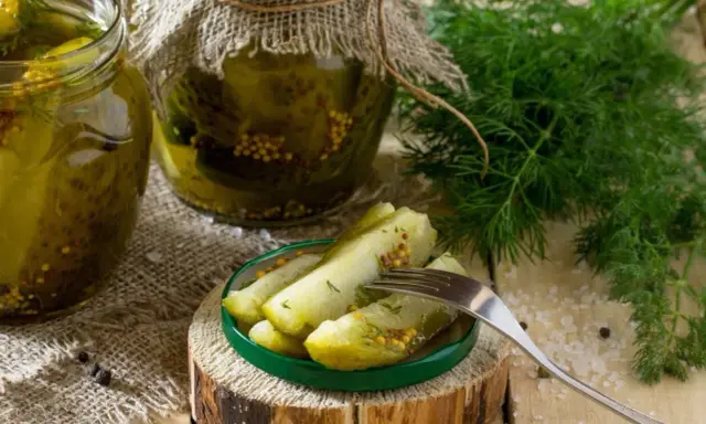 Słoiki z ogórkami w musztardzie, świeży koperek i widelec z kawałkami ogórka na talerzyku.