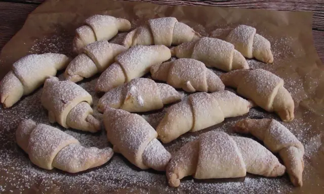 Pyszne rogaliki serowe 3 składnikowe, posypane cukrem pudrem, ułożone na papierze do pieczenia.
